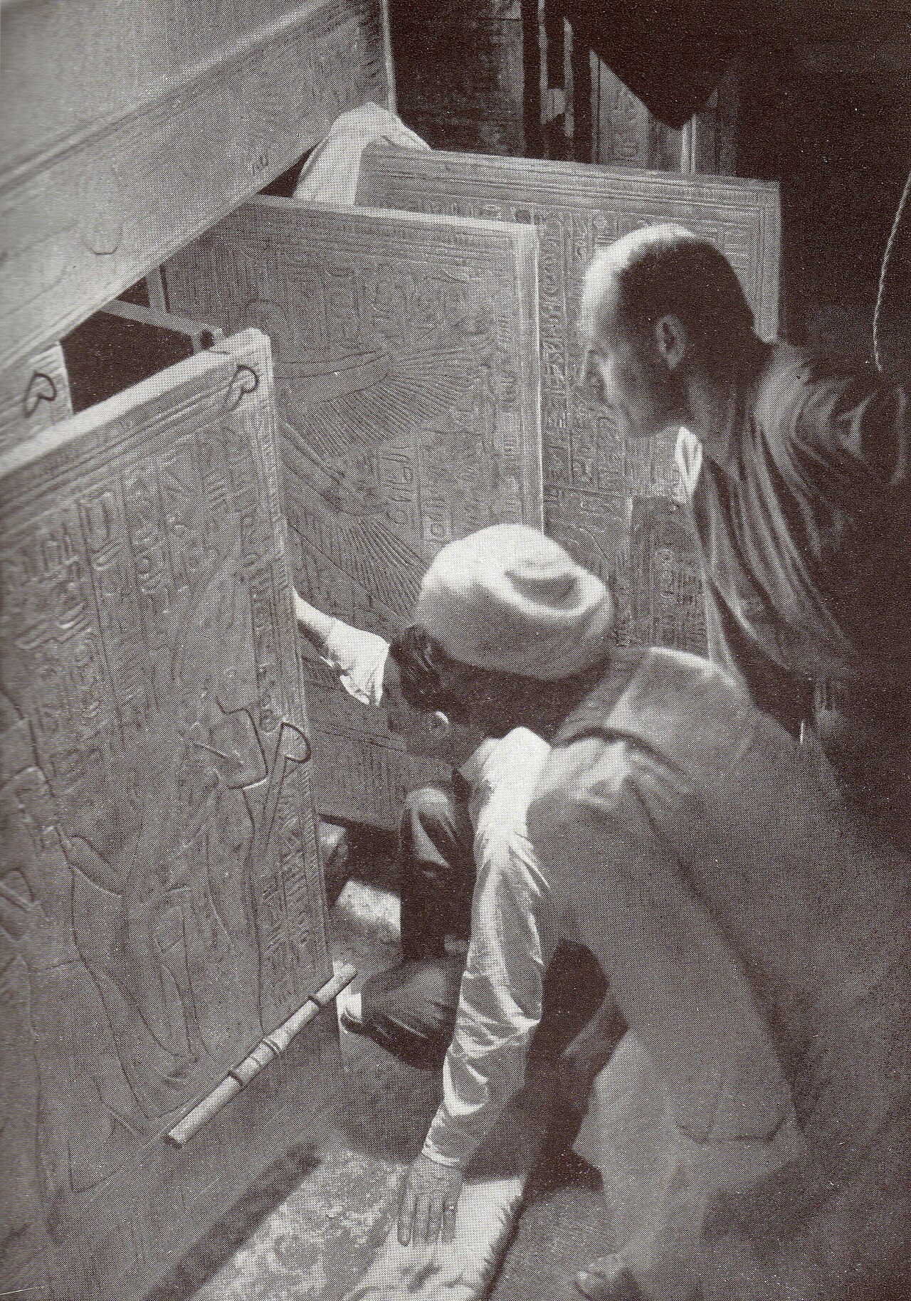 Black-and-white photograph of Howard Carter kneeling at the open doors of a burial shrine inside Tutankhamun’s tomb, beside two colleagues.