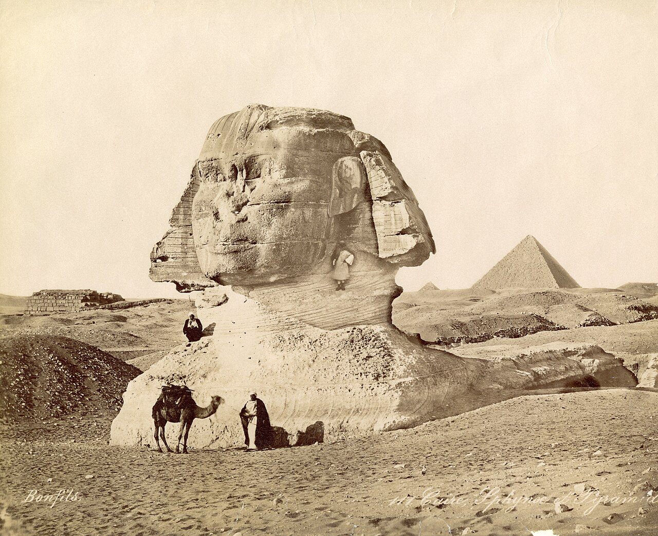 Nineteenth-century photograph of the Great Sphinx of Giza, buried in sand up to its chest, with a pyramid in the distance.